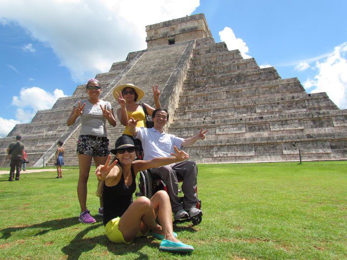 Ricardo Shimosakai está acompanhado de mais 3 pessoas, numa parte gramada em frente ao monumento Chichen Itzá no México